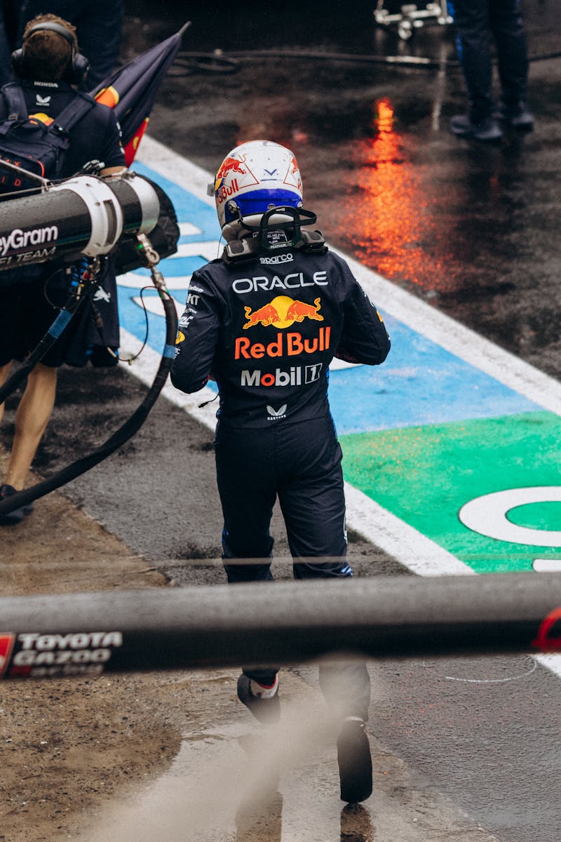Action shot of a Formula 1 driver in the pit lane, showcasing team branding during a wet race day.