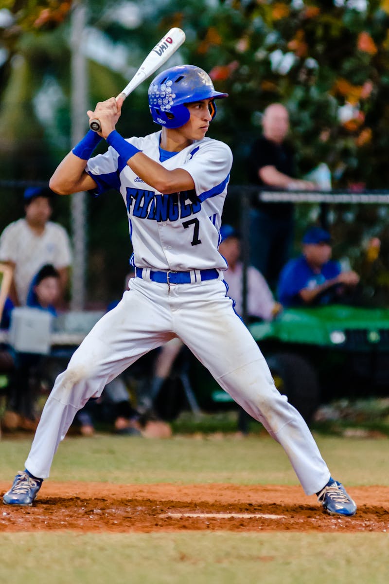 Teen baseball player in uniform ready to swing during a game on a grassy field.